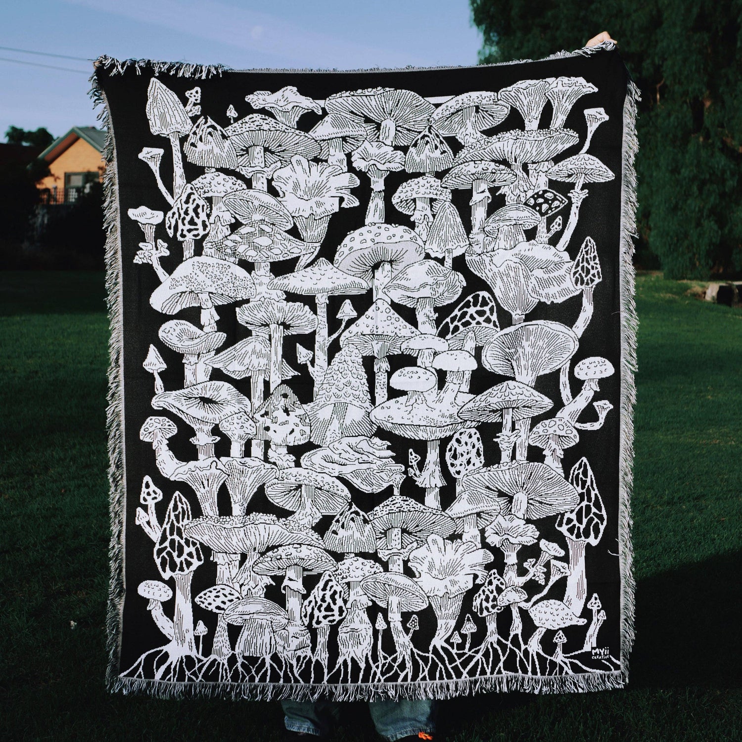 Black blanket with white mushroom pattern held by a person outdoors